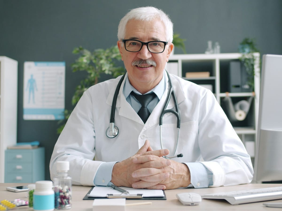 Senior physician in a white coat seated at his office desk