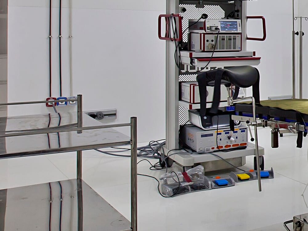 An operating-room equipment cart with a stacked camera control unit, processor, and radiofrequency generator console, with footswitches and cables