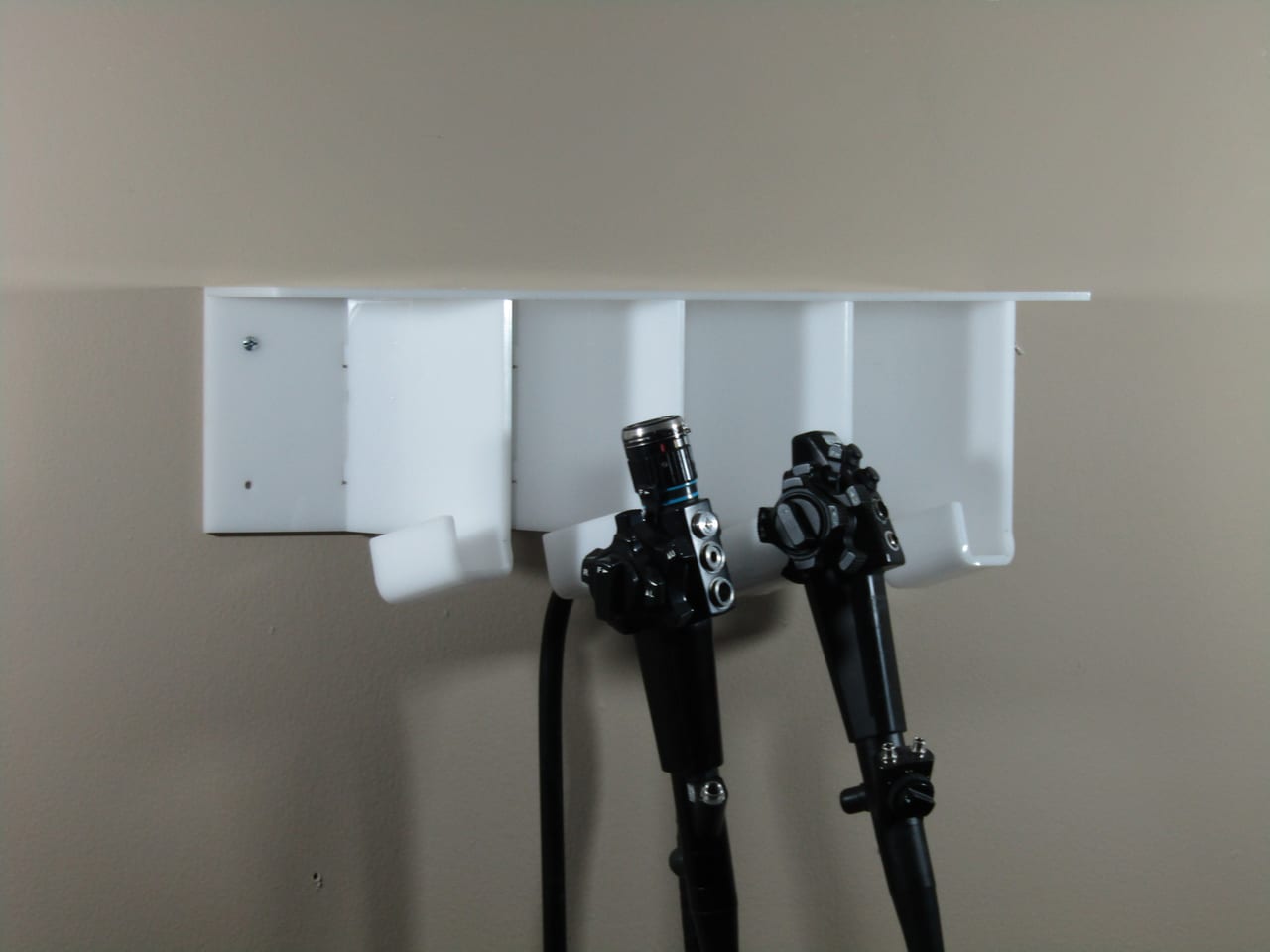 Two used flexible endoscopes hung by their control heads on a wall-mounted storage rack, their insertion tubes hanging down, showing normal wear from prior clinical use