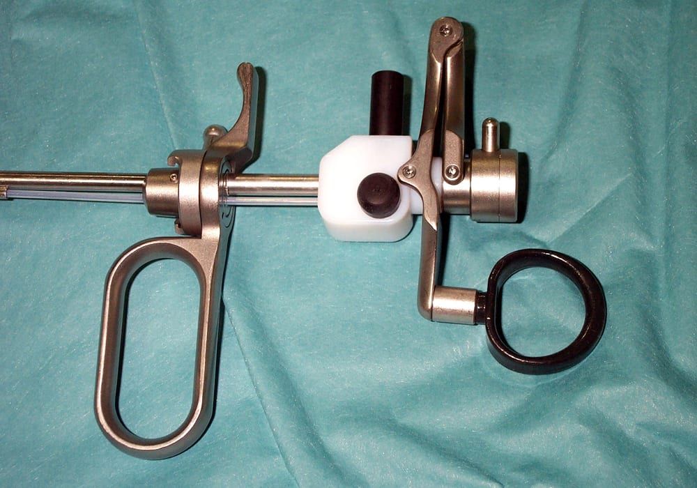 A used rigid endoscopic surgical instrument — a resectoscope working element with a finger-ring handle, spring mechanism, and telescope shaft — laid on a surgical drape, showing normal wear from prior clinical use
