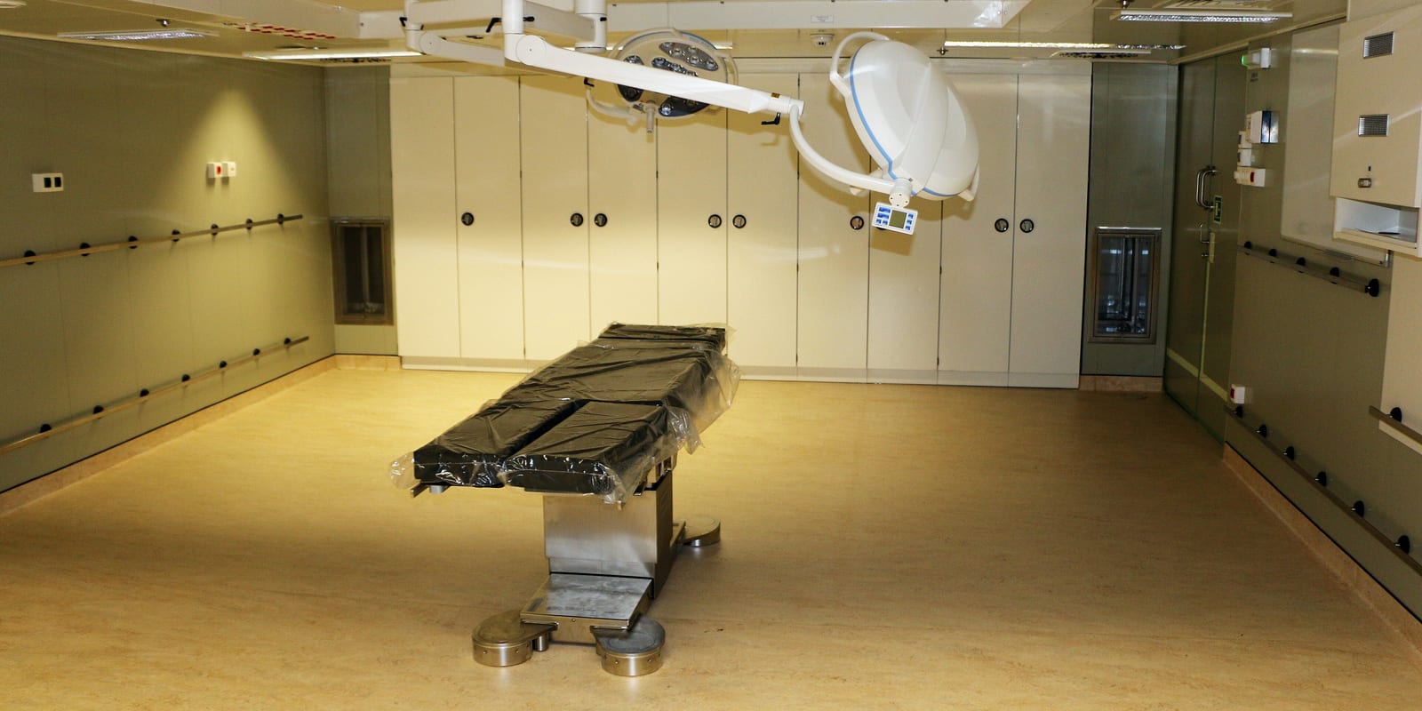 Empty operating room: plastic-wrapped operating table under two ceiling surgical lights, white cabinet wall