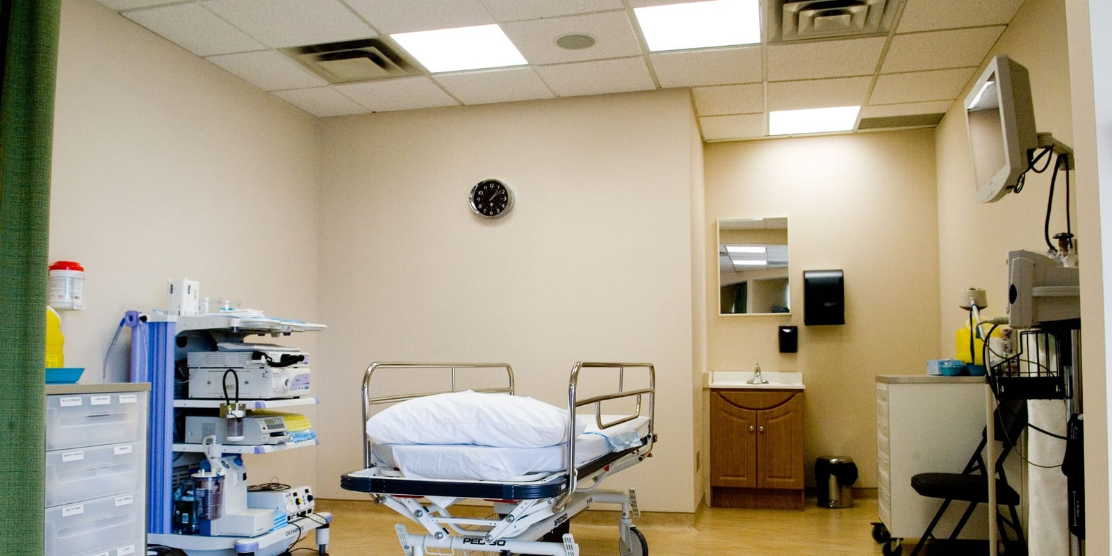 Endoscopy procedure room: empty stretcher with pillow, endoscopy tower, wall clock, sink, drawer unit