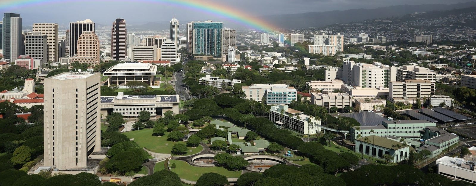 Downtown Honolulu towers and the Hawaii State Capitol under a rainbow