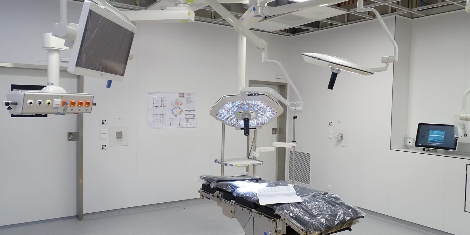 New operating room: plastic-wrapped table, lit LED surgical light, ceiling pendants and boom monitor