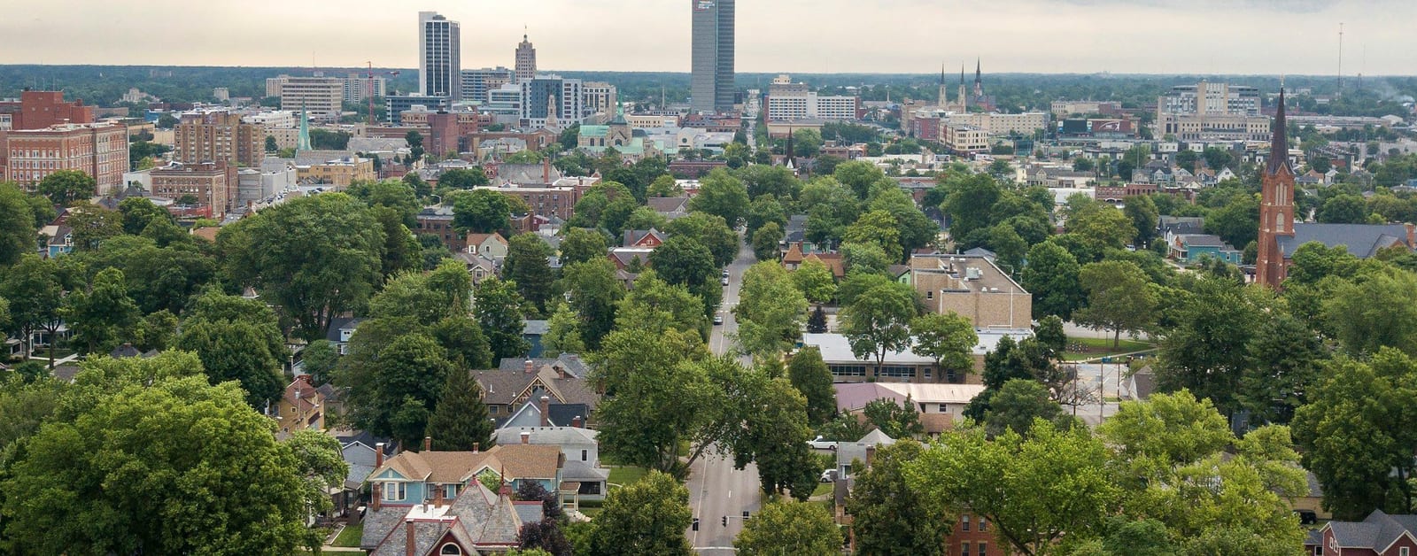Aerial view of downtown Fort Wayne's skyline beyond tree-lined neighbourhoods under storm clouds