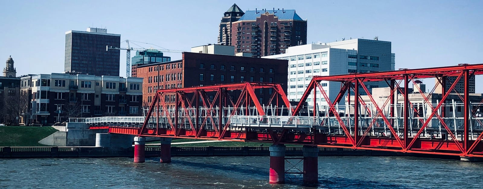 Red truss footbridge over the Des Moines River with downtown Des Moines behind