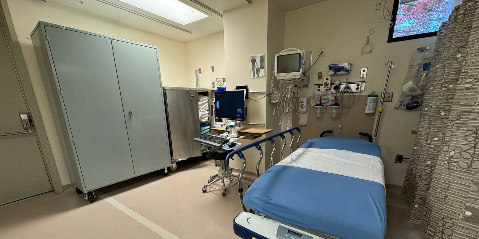 Procedure preparation bay: empty stretcher, wall gas outlets and monitor, steel cabinets, workstation