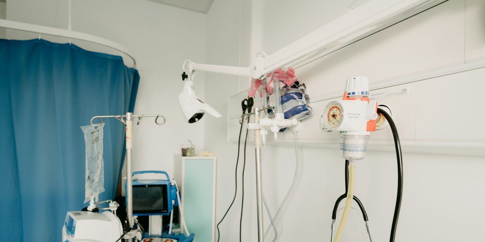 Room corner with IV pole and bag, infusion pump, vitals monitor stand, suction regulator and wall lamp