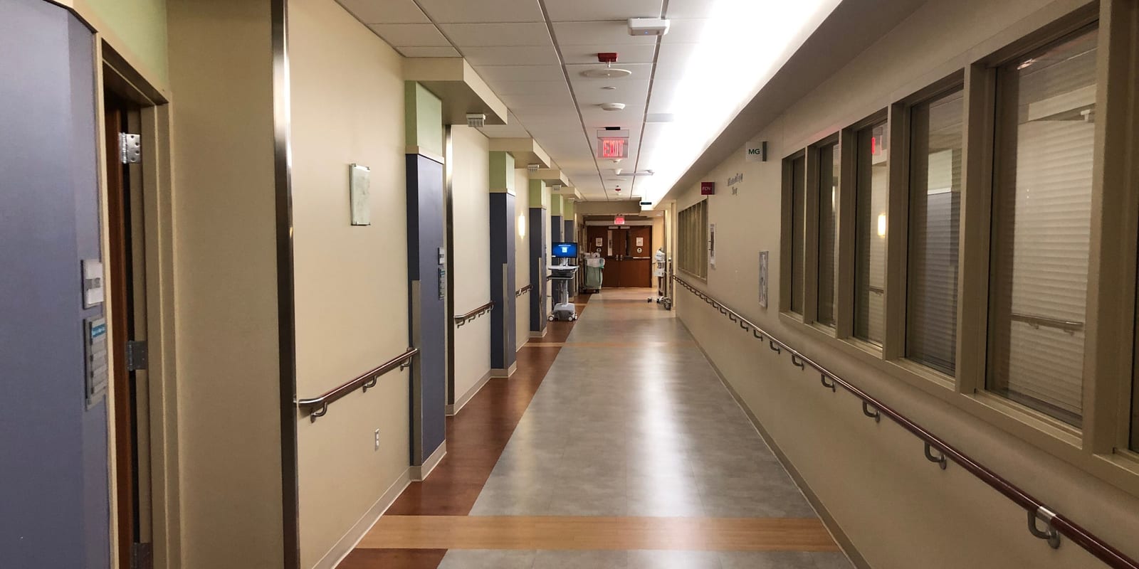 Ward corridor with handrails, a window wall and room doors, a computer cart at the far end