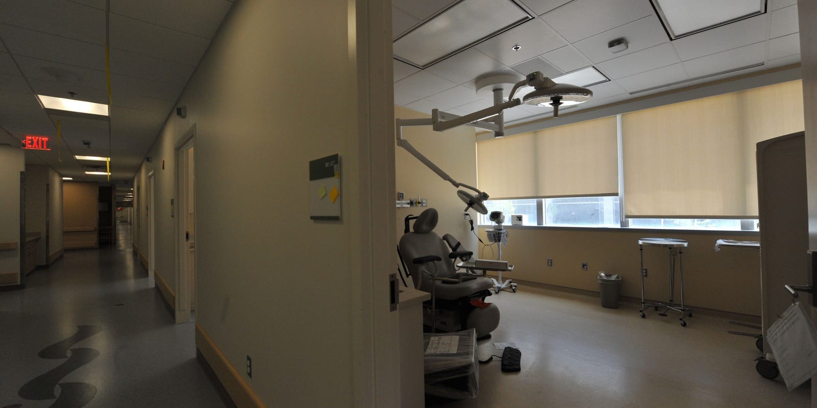 Corridor beside an empty treatment room with exam chair, ceiling surgical light and instrument stands