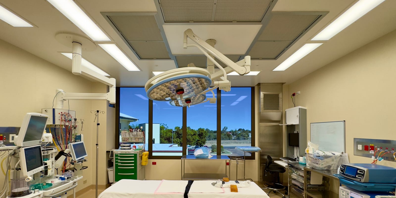 Operating room: surgical light over made-up table, anaesthesia monitors, trolleys, large window to trees