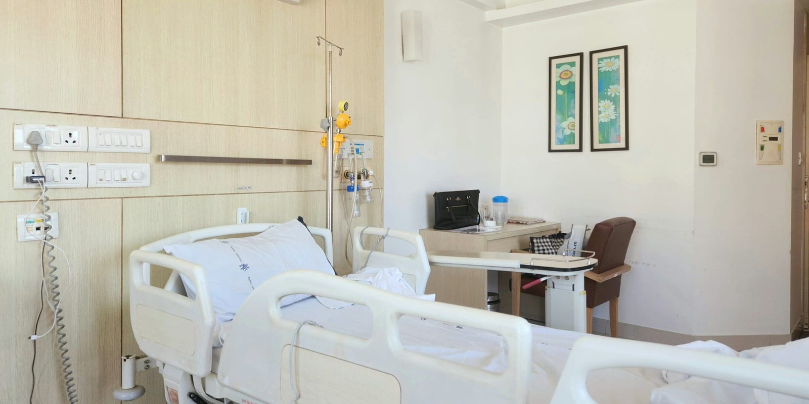 Empty adjustable hospital bed with side rails beside a wood-panelled headwall and IV pole