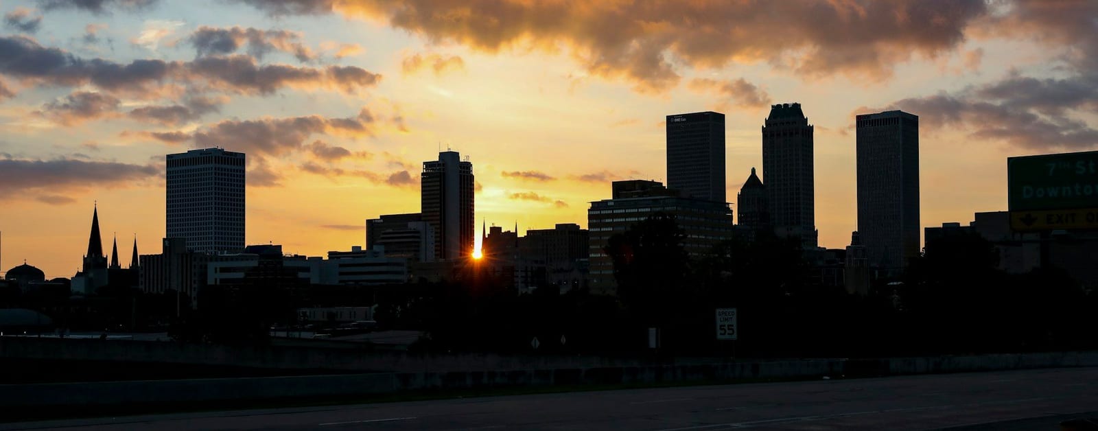 Silhouetted downtown Tulsa skyline at sunset seen from the highway