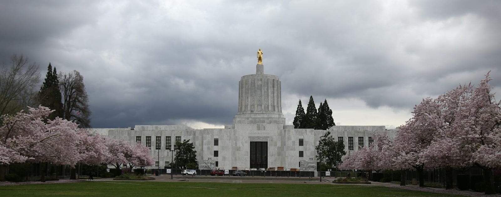 Oregon State Capitol in Salem with its gold pioneer statue, framed by cherry blossoms