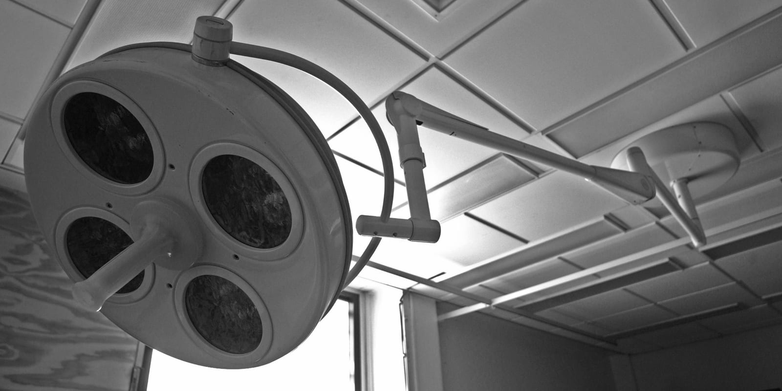 Multi-lamp surgical light on articulated ceiling arm, coffered ceiling, window light behind