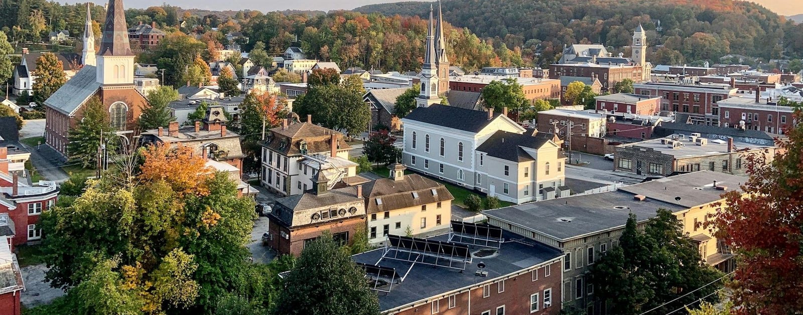Elevated view of downtown Montpelier rooftops and church steeples among autumn trees and hills