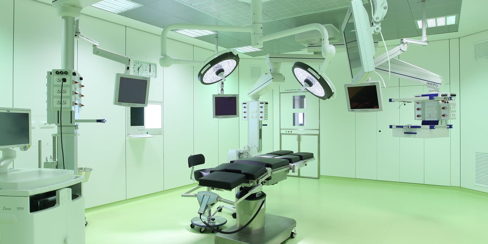 Large modern operating room: operating table, twin surgical lights, ceiling pendants, monitors
