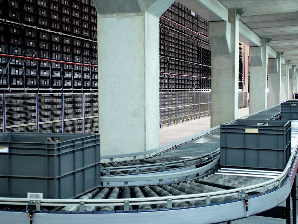 Totes travelling on a curved roller conveyor beside high density bin storage