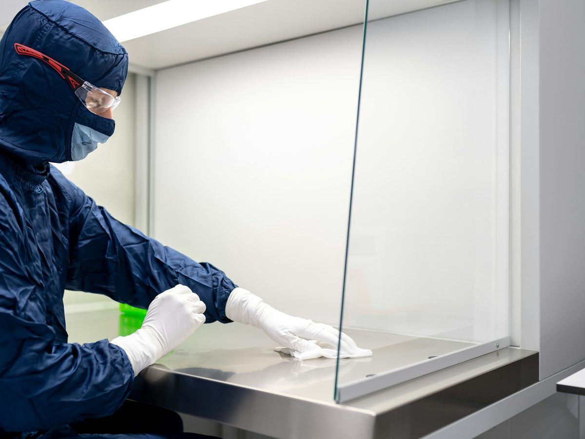 Technician wiping the work surface of a biological safety cabinet behind its glass sash