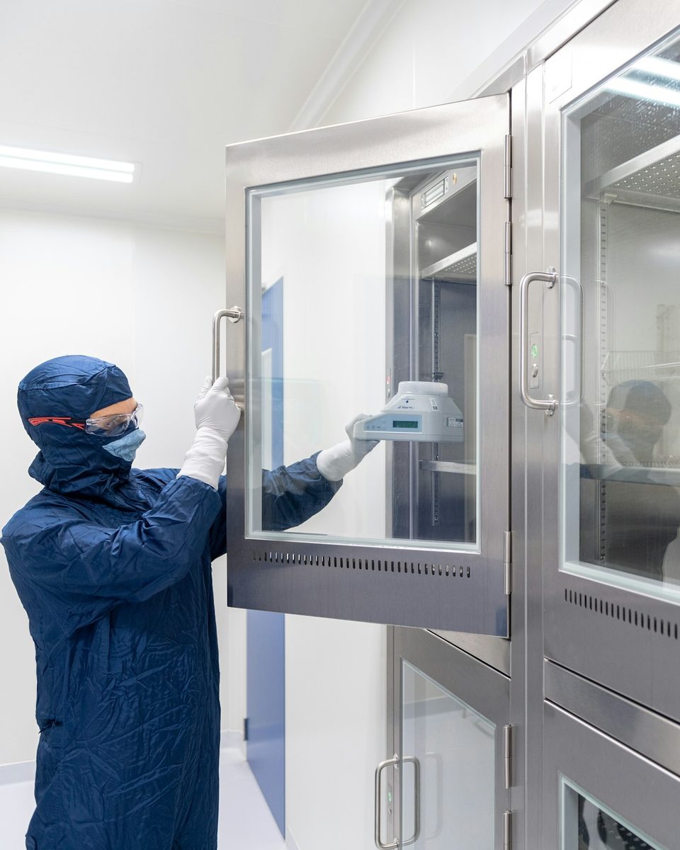 Gowned technician loading a stainless steel cleanroom cabinet