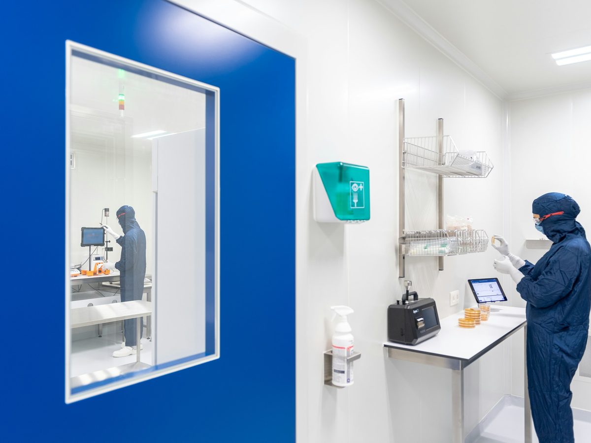 Cleanroom with a vision panel door, wall mounted fixtures and a gowned technician