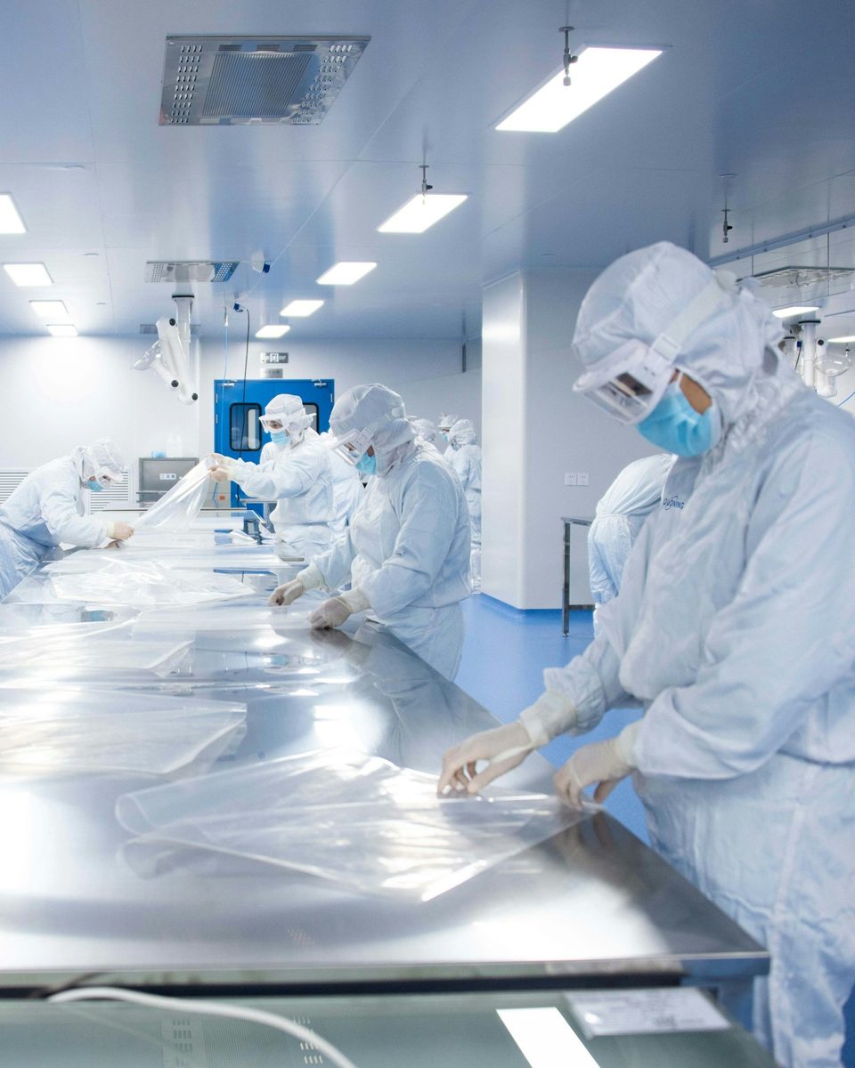 Gowned technicians working at stainless steel tables in a large cleanroom