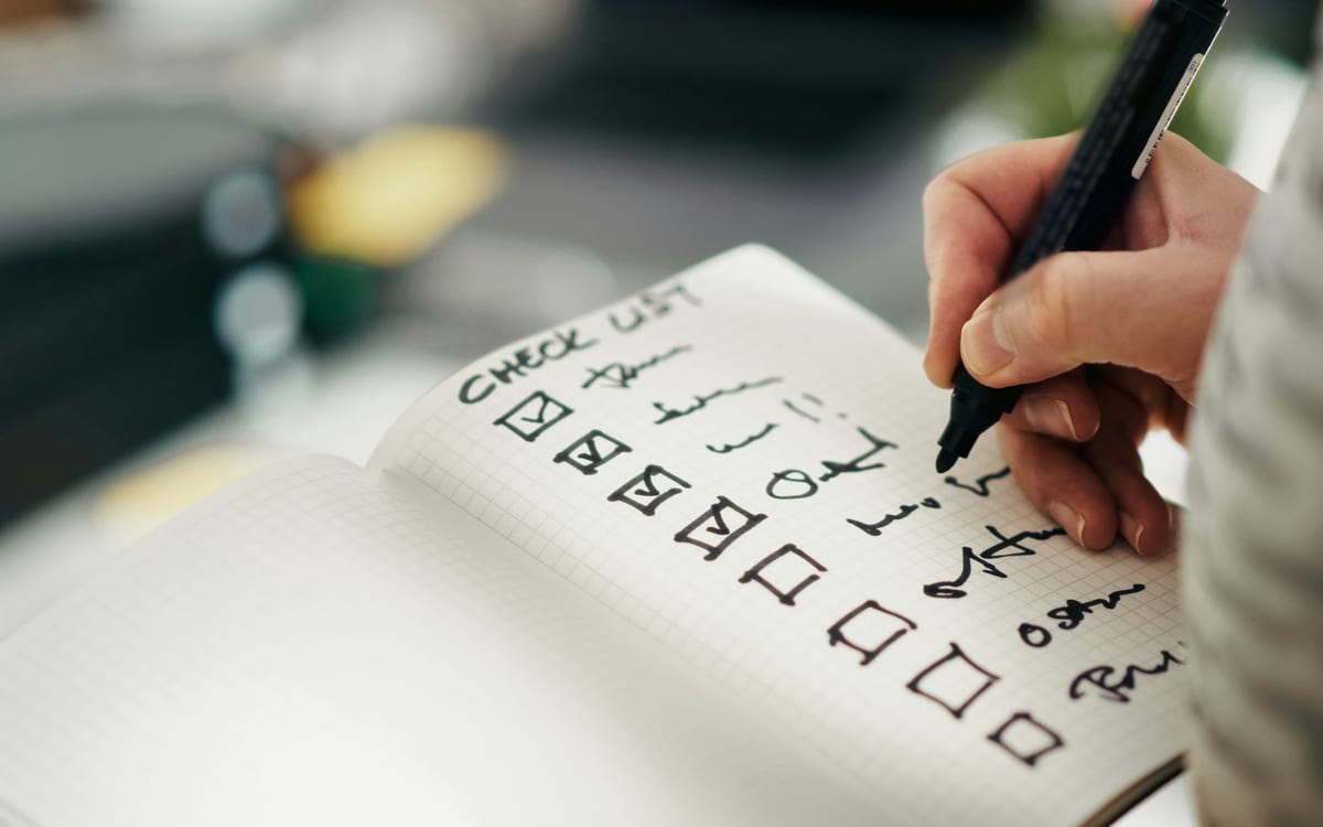 A hand ticking off items on a handwritten checklist