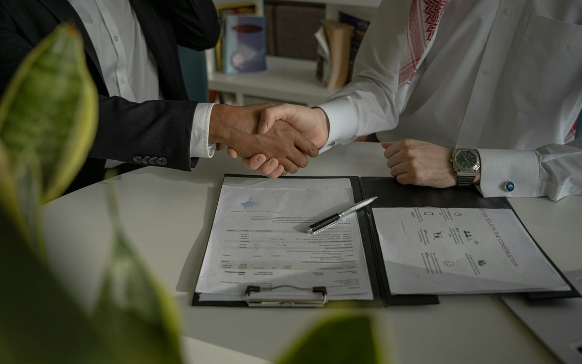 Two people shaking hands over a signed agreement on a desk