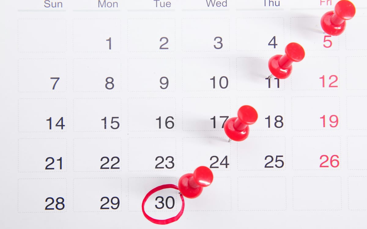 A wall calendar with dates marked by red pushpins and one date circled